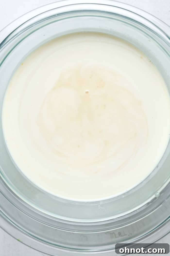 Heavy whipping cream and vanilla extract added to the cooled custard mixture in a bowl.