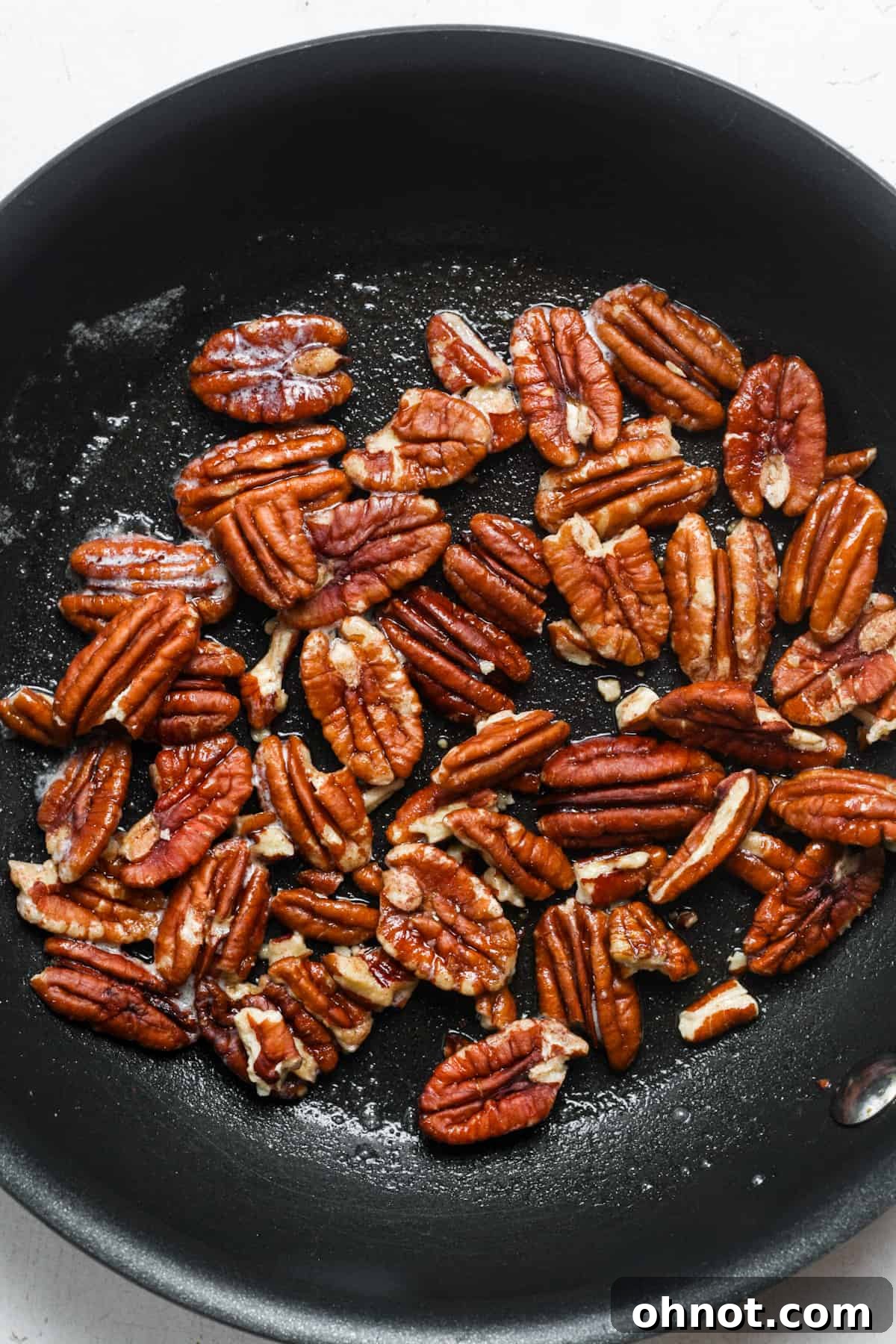 Pecan pieces being toasted in butter in a skillet.
