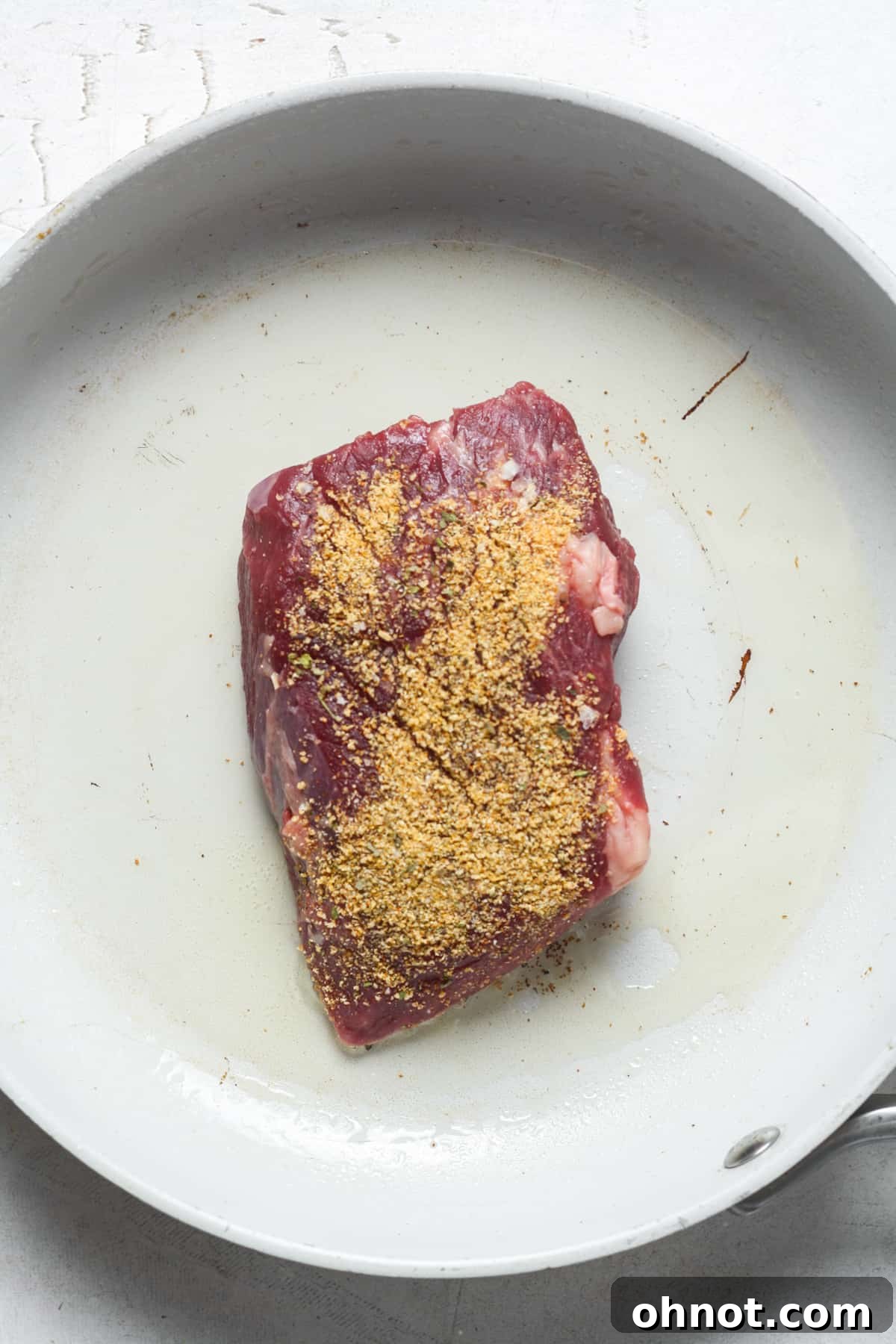 Denver steak searing in a white skillet, developing a crust.