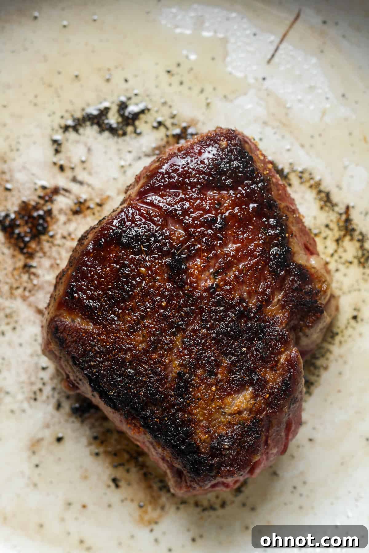 Close-up of a thick, seasoned Denver steak cooking in the pan.