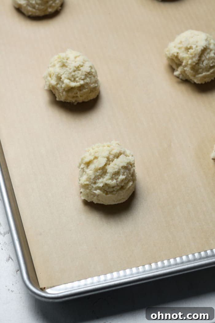 Unbaked lemon ricotta cookie dough balls on a parchment-lined pan.