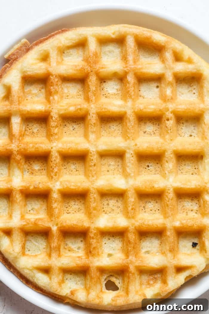 A perfectly cooked golden crispy waffle being removed from the waffle maker.