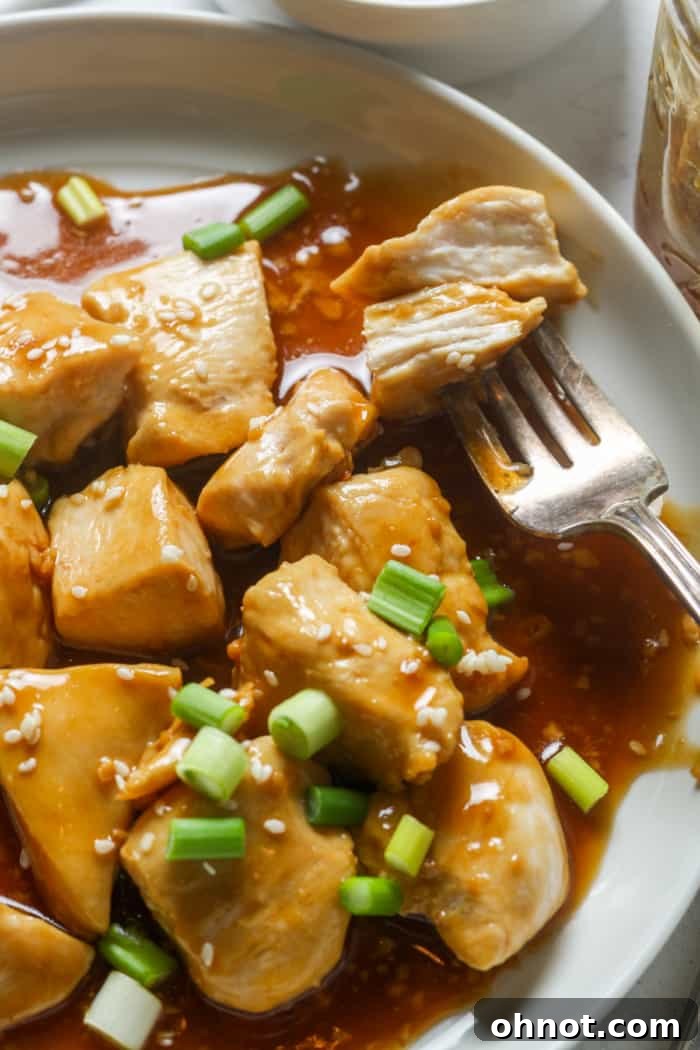 A serving of sticky Chinese garlic chicken garnished with sesame seeds and green onions.