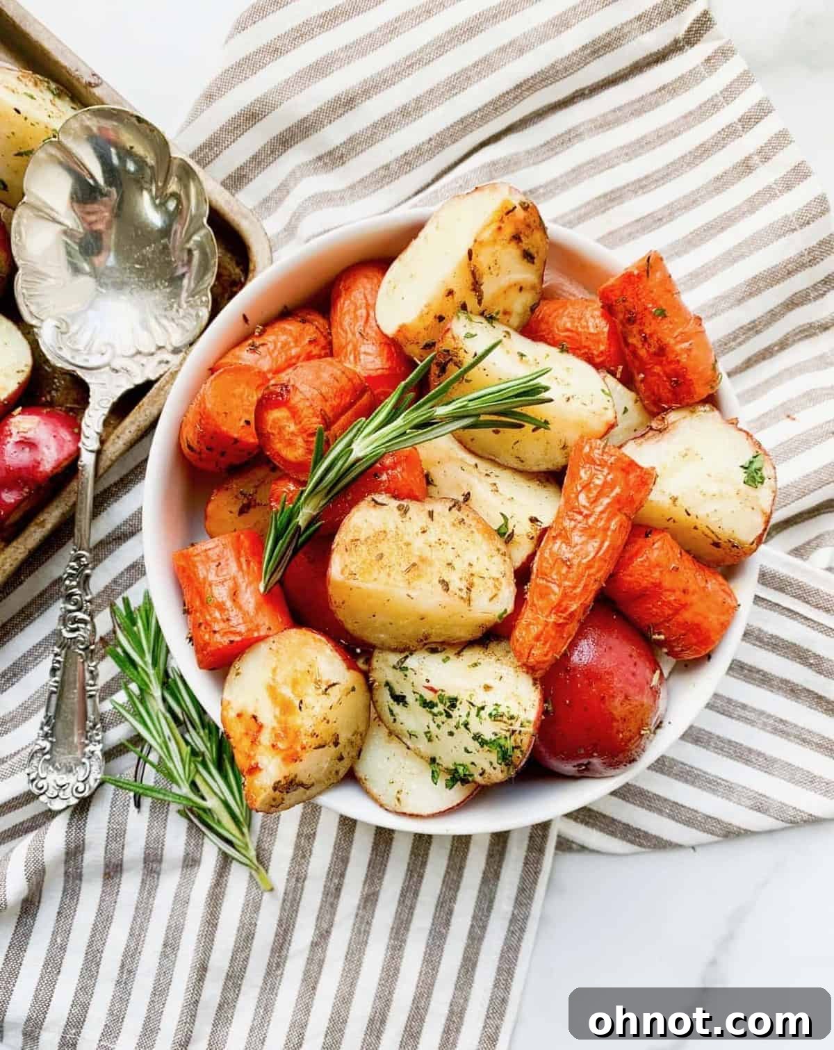 Close-up of golden brown roasted potatoes and carrots garnished with fresh rosemary on a baking sheet.