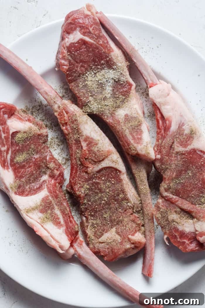 Raw lamb chops seasoned with salt and pepper, showing the frenched bones.