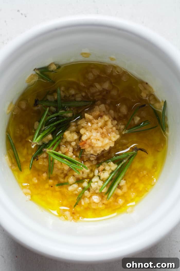 A small bowl containing olive oil, minced garlic, and chopped rosemary, ready to be mixed.
