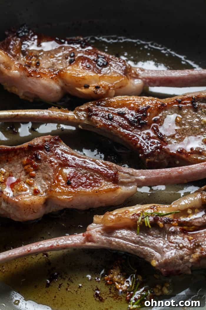 Close-up of seared lamb lollipops in a skillet, showing the crispy exterior.