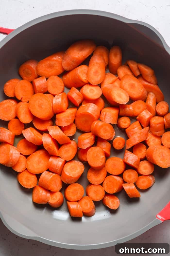 Sliced carrots cooking in a lidded skillet with olive oil.