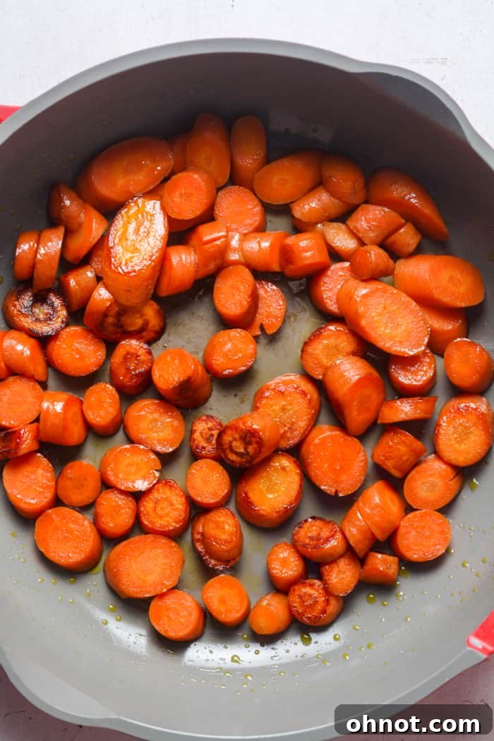 Partially cooked carrots being stirred in a skillet.