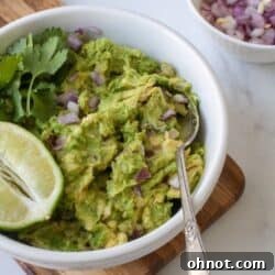 Bowl of guacamole with cilantro, onions and lime