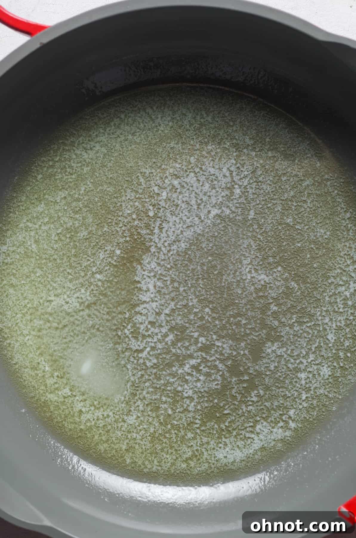 Unsalted butter melting in a large skillet over medium heat, forming a clear liquid.