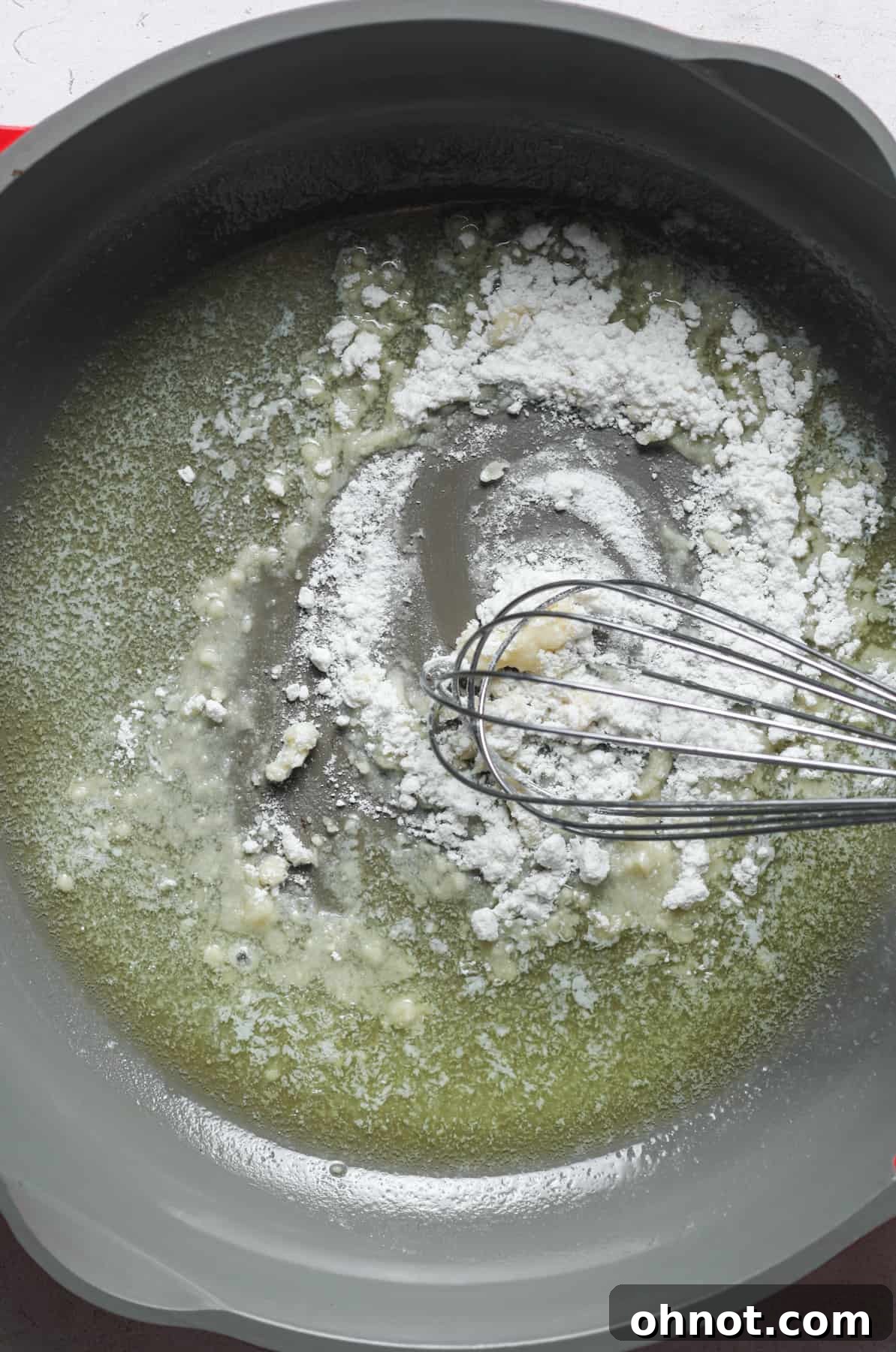 Flour being whisked into melted butter in a pan, creating a creamy roux.