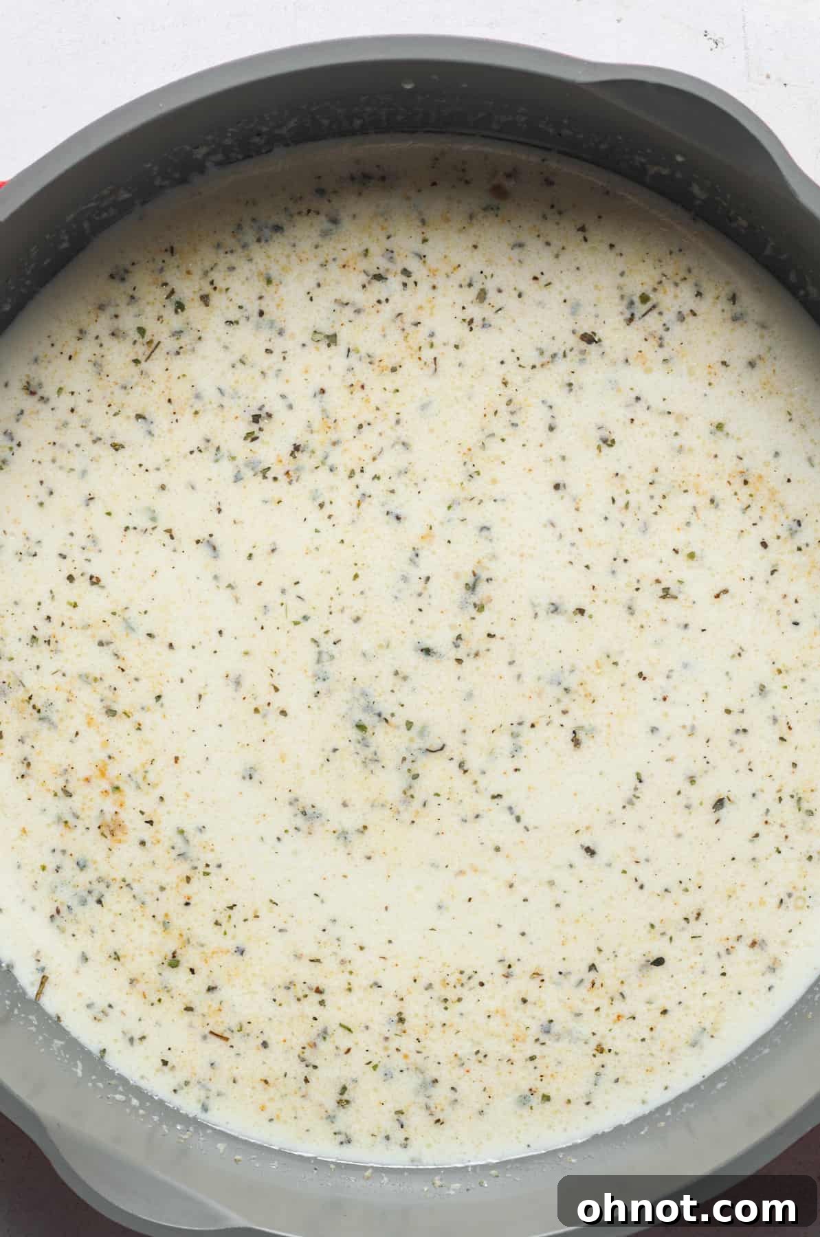 A creamy white sauce simmering gently in a pan, infused with spices.