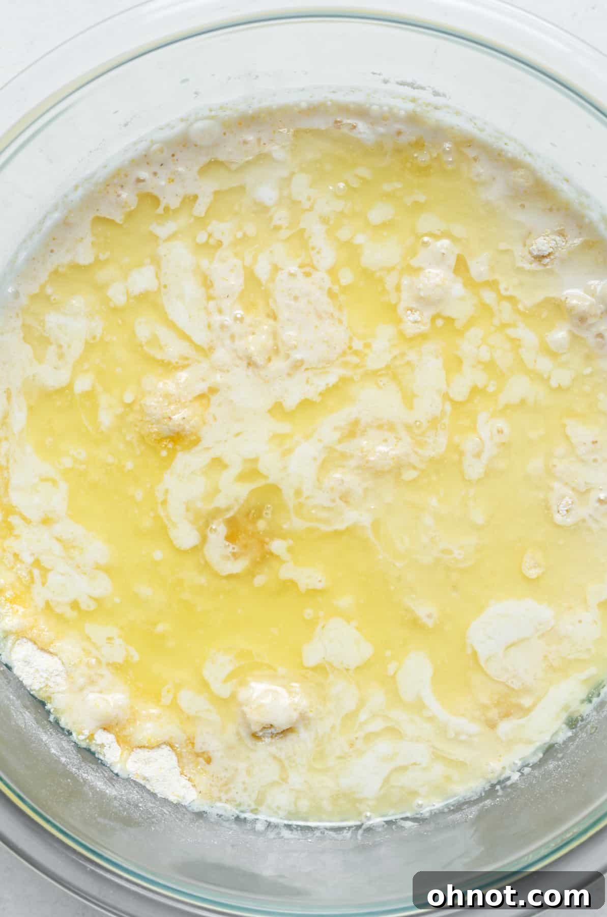 Close-up of a mixing bowl with melted butter being added to the dry flour and cornmeal mixture, showing the initial integration of wet and dry ingredients.