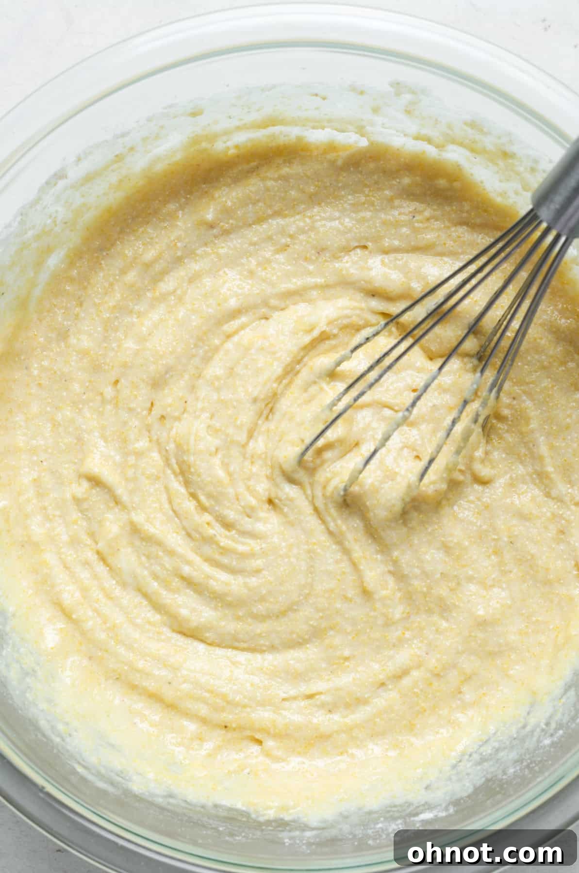 A close-up of thick, yellow cornbread batter in a mixing bowl, showcasing its smooth consistency and readiness for baking.