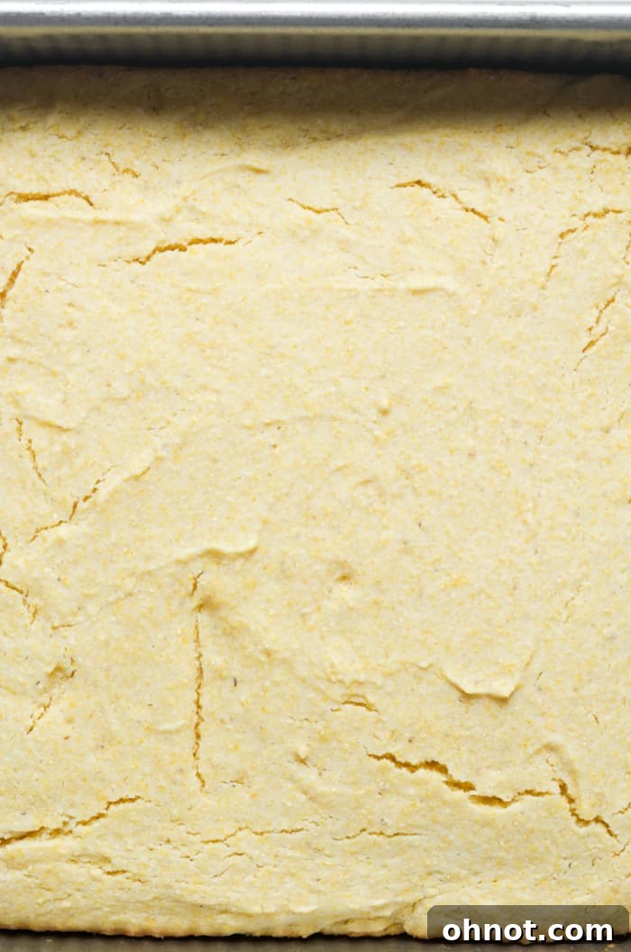 A freshly baked, golden-brown gluten-free cornbread in a square baking pan, showing a perfectly risen and inviting crust.