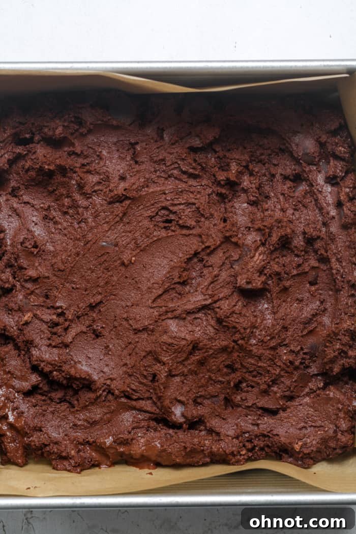 Greek yogurt brownie batter meticulously spread into an even layer in a parchment-lined baking pan.