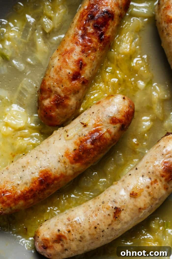 Bratwurst simmering in a skillet with onions.