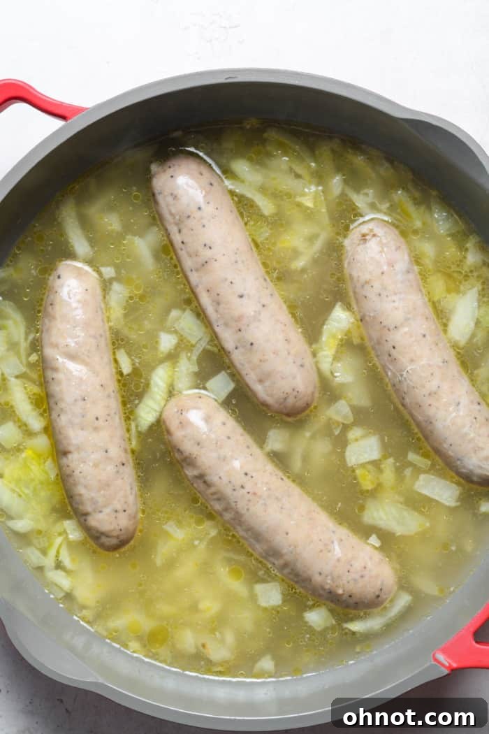 Bratwurst sausages placed in a skillet with onions and covered with broth.