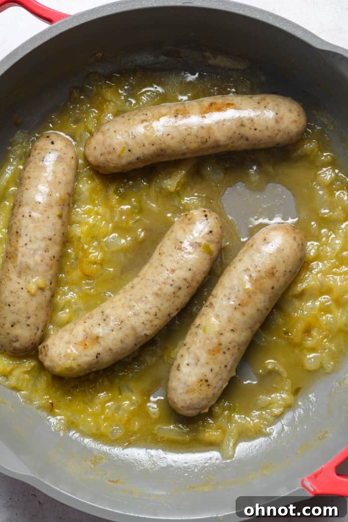 Bratwurst simmering with caramelized onions in a skillet.