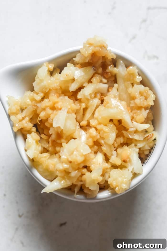 Bowl of freshly minced garlic, ready to be used or stored, with garlic cloves in the background.