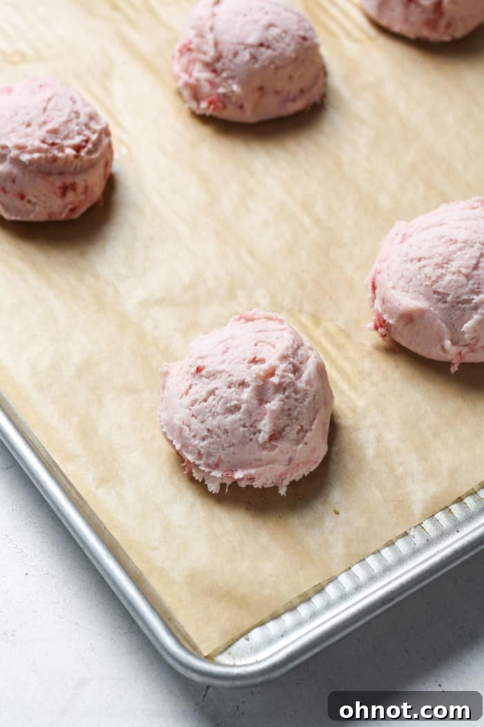 Pink balls of cookie dough on a parchment-lined baking sheet.