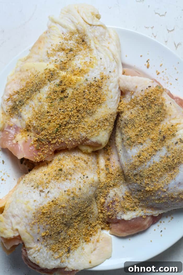 Close-up of raw chicken thighs in a bowl, coated with a generous layer of seasoning.
