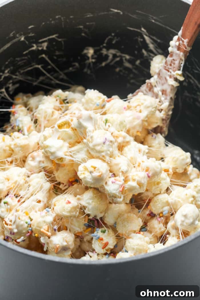 Colorful sprinkles being added to the marshmallow-coated popcorn mixture.