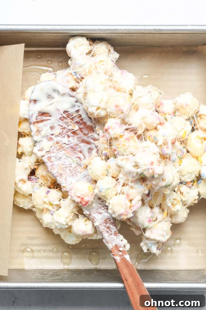 Popcorn mixture being pressed into the lined baking pan with a wooden spoon.
