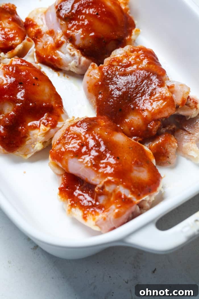 Chicken thighs arranged in a baking dish with initial BBQ sauce coating.