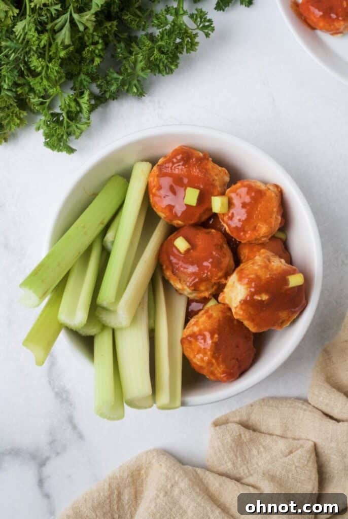 Close-up of Whole30 chicken meatballs coated in vibrant buffalo sauce, glistening in a skillet.