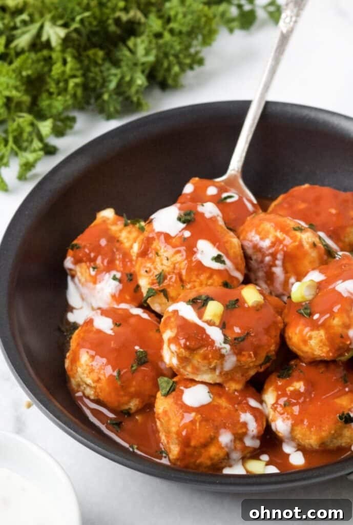 Paleo buffalo chicken meatballs simmering in a cast iron skillet, coated in spicy sauce.