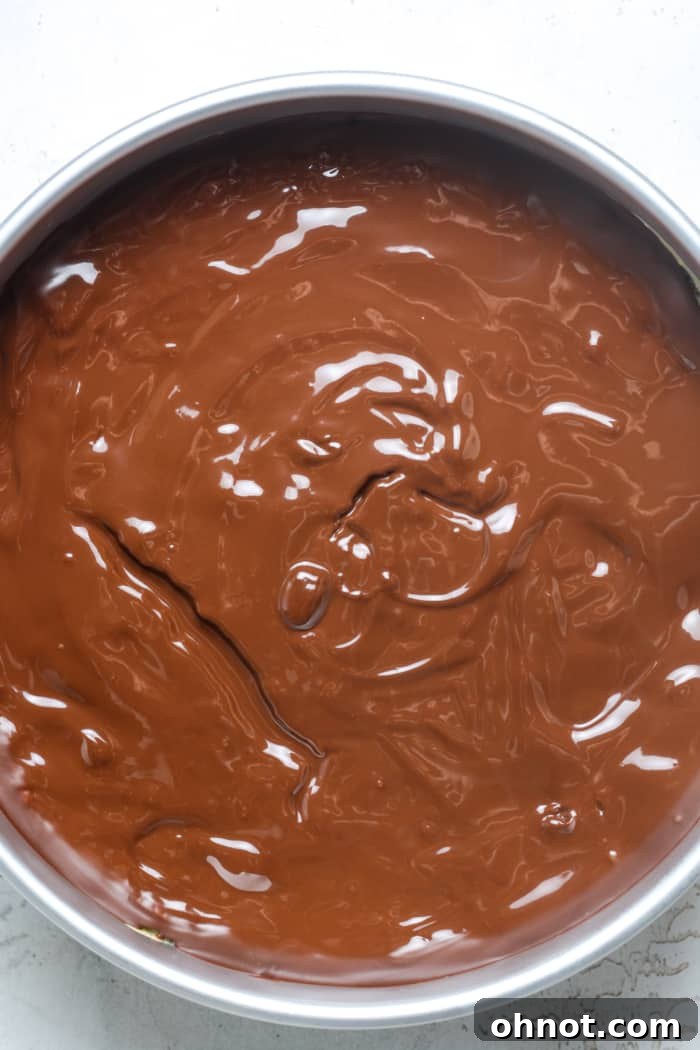 A springform pan with a finished Oreo cheesecake topped with a smooth layer of chocolate ganache, chilling to set.