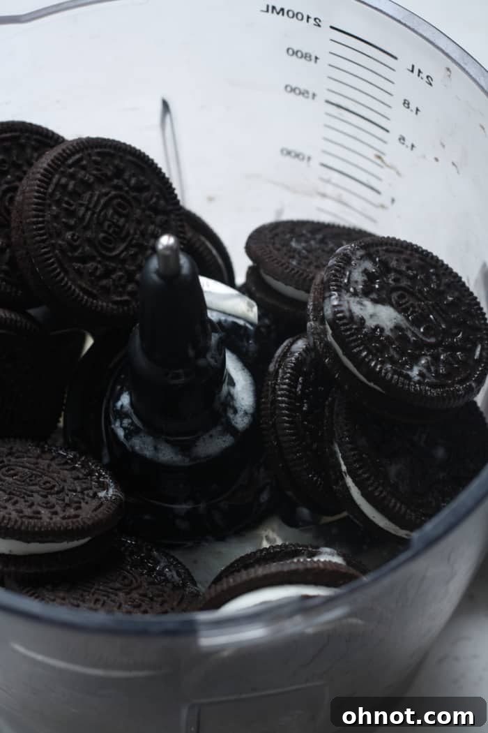 Oreo sandwich cookies being added to a food processor to make the crust.