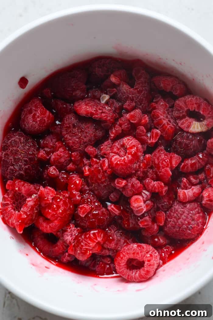 Thawed frozen raspberries in a bowl, showing their juice.