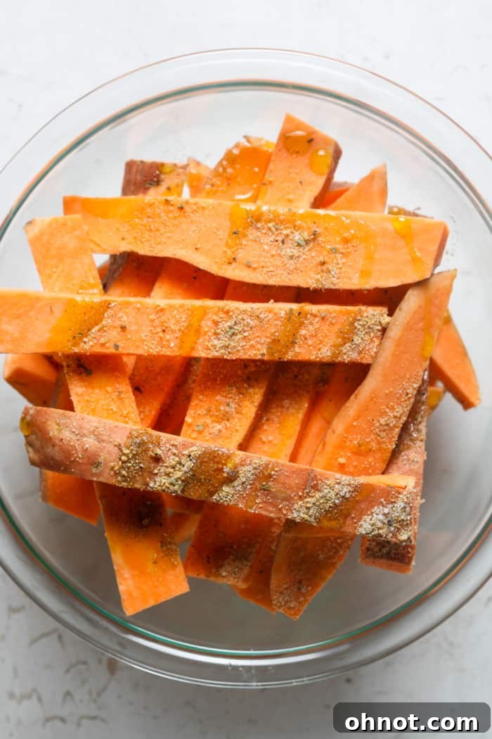 Sliced sweet potato fries coated in seasonings within a mixing bowl.