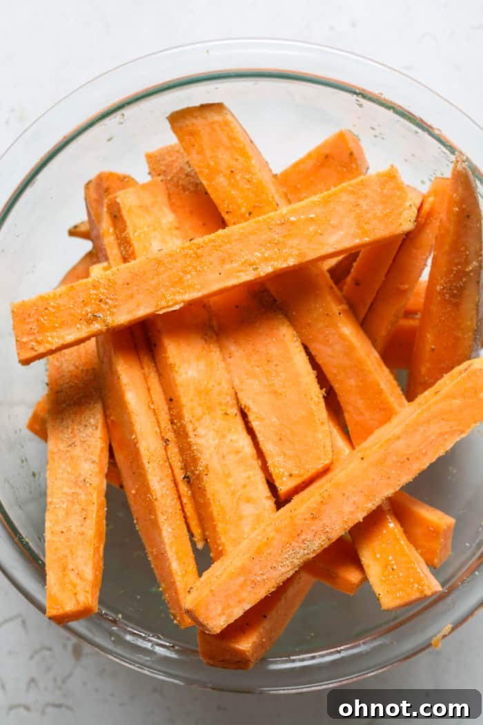 Orange-colored seasoned sweet potato fries in a bowl, ready for the air fryer.