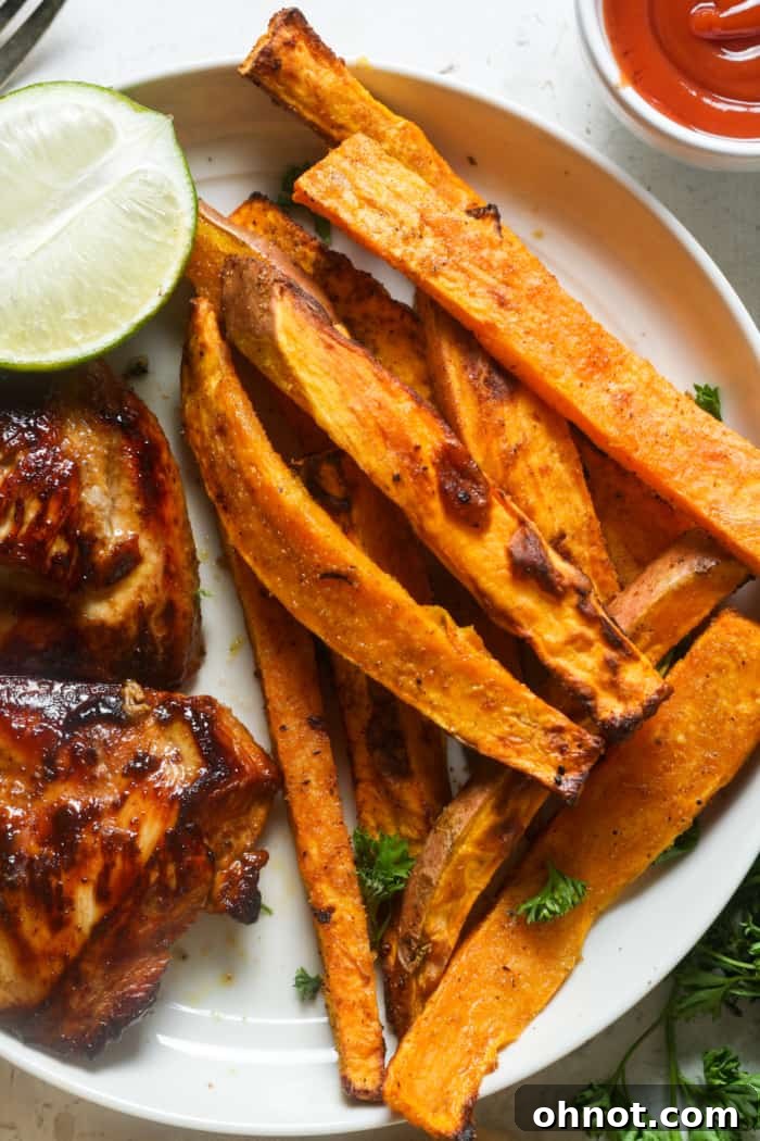 Grilled chicken and crispy sweet potato fries on a plate, showcasing a complete meal.