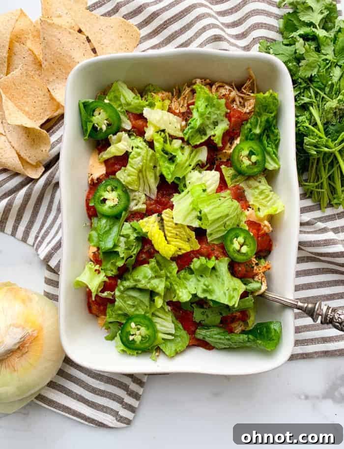 A beautifully arranged white casserole dish showcases a vibrant, multi-layered taco dip, ready for scooping.