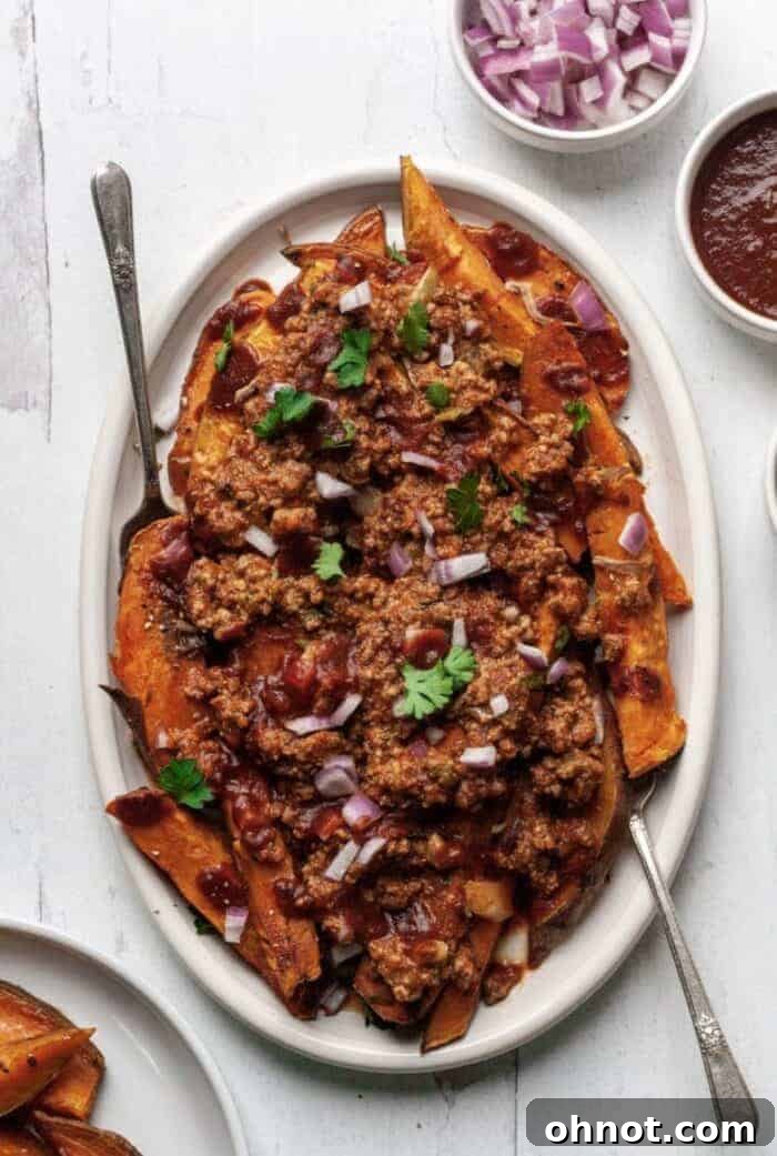 A white plate generously topped with perfectly cooked sweet potato fries and a rich, savory homemade chili.