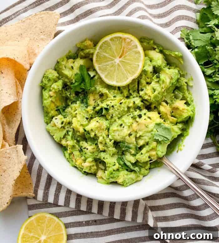A vibrant green bowl of freshly made guacamole rests on a stylish gray and white striped towel, ready to be enjoyed.