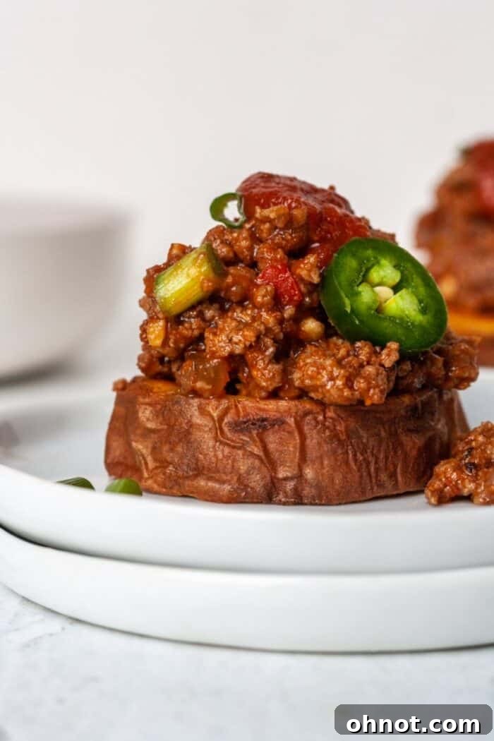 A delectable Sloppy Joe mixture served atop a roasted sweet potato slice, presented on a clean white plate for a hearty and healthy meal.