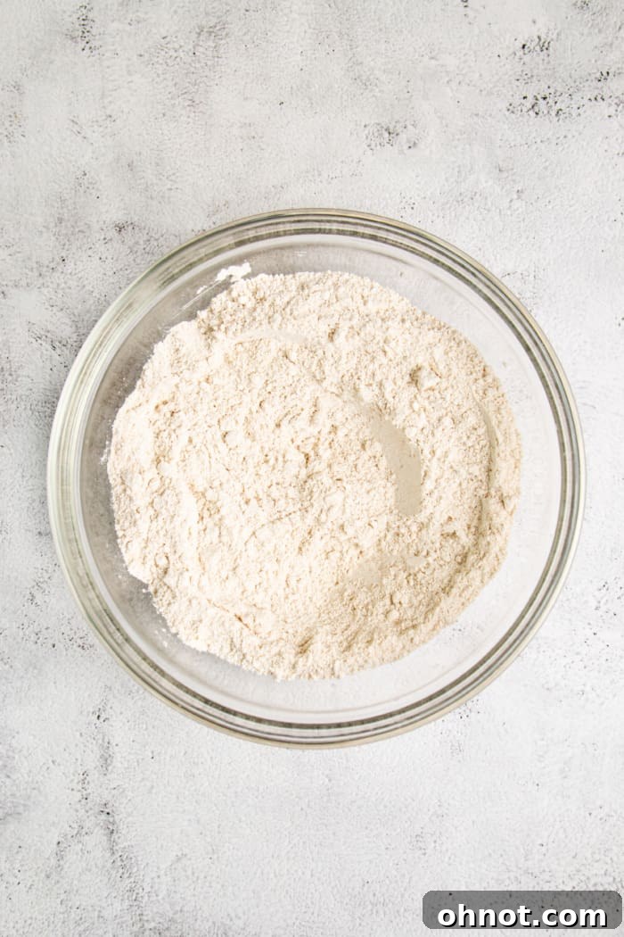 Various gluten-free flours and dry ingredients measured into a large mixing bowl, ready to be whisked together.