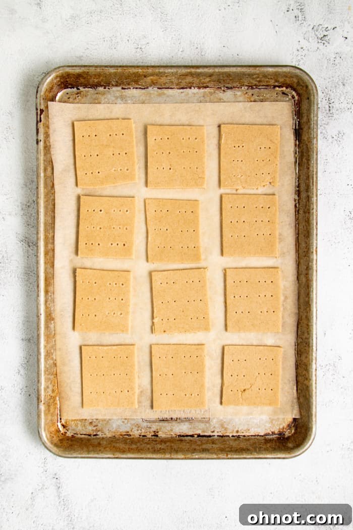 Unbaked graham crackers neatly arranged on a parchment-lined baking sheet, with small gaps between them, ready for the oven.
