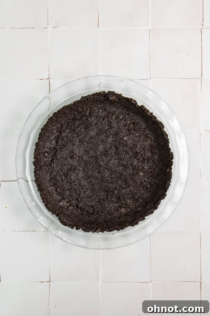A freshly pressed Oreo cookie crust in a glass pie dish, chilling in the fridge.