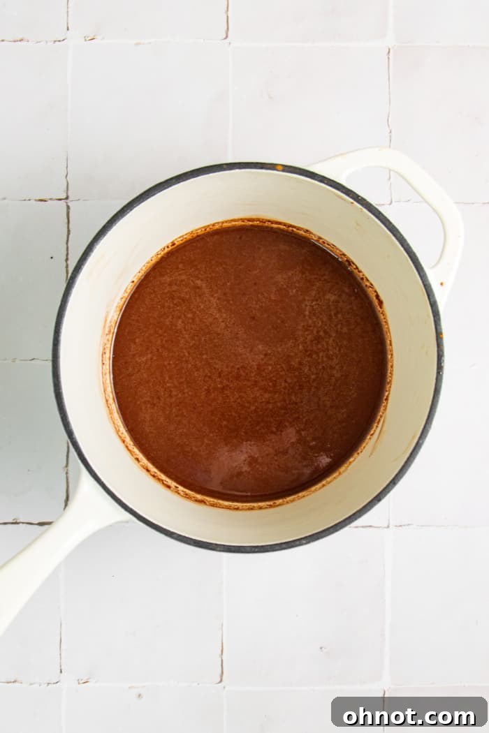 Rich, glossy chocolate ganache being stirred in a small saucepan.