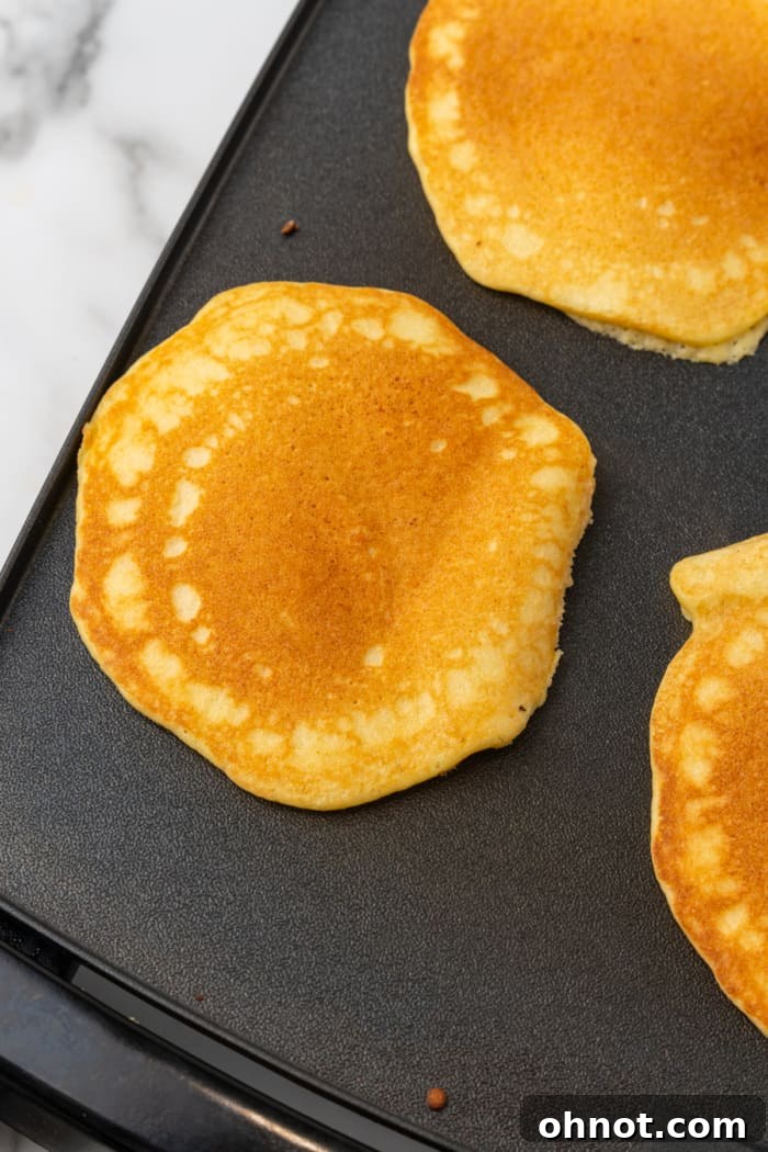 Golden keto pancakes cooking on a griddle.