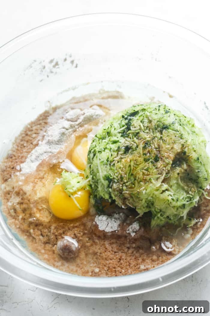 Close-up of shredded zucchini, eggs, and coconut sugar in a mixing bowl.