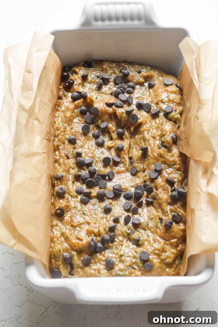 Raw zucchini bread batter in a lined bread pan, topped with extra chocolate chips.