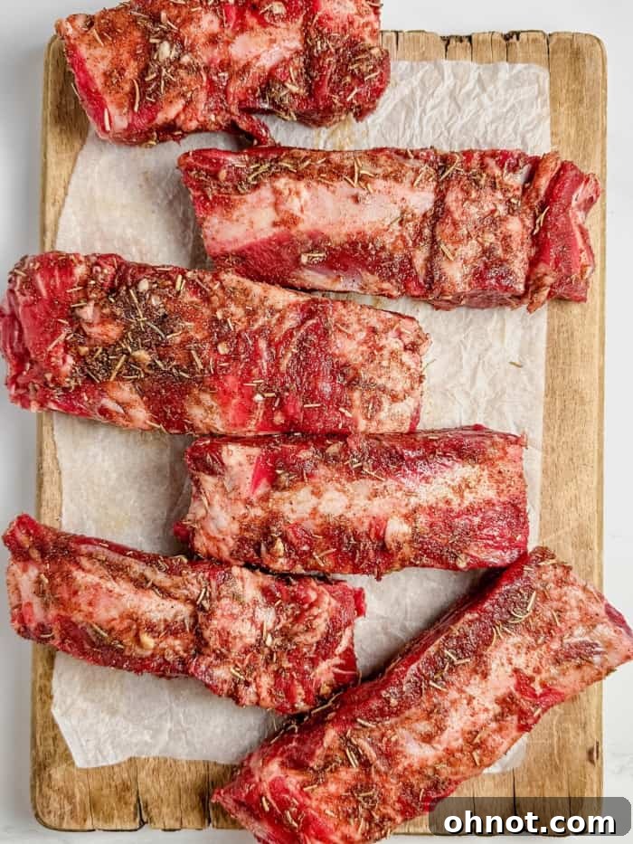 Pieces of beef ribs on a cutting board, thoroughly coated with dry rub.
